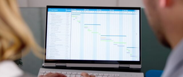 Dos profesionales analizando la planificación de un cronograma en un diagrama de Gantt en la pantalla de una laptop para la gestión de proyectos de innovación empresarial, enmarcado como imagen principal para una entrada de blog.