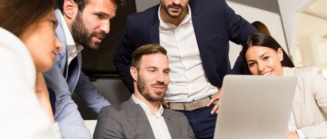 Equipo de profesionales reunidos alrededor de una laptop, colaborando en la revisión digital de avances para la gestión ágil de proyectos y la innovación empresarial, presentado como imagen principal para una entrada de blog.