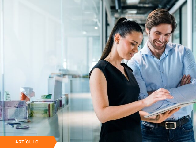 Imagen de portada para artículo técnico que muestra a dos profesionales en un pasillo de oficina moderno revisando datos en una tablet, con una etiqueta naranja de ARTÍCULO en la esquina inferior izquierda.