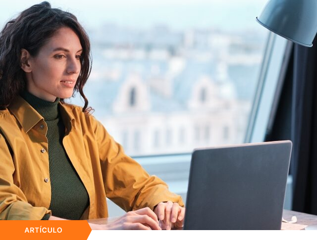 Imagen de portada para artículo mostrando a una profesional trabajando en su laptop frente a un ventanal al atardecer, con una etiqueta naranja de ARTÍCULO en la esquina inferior izquierda.