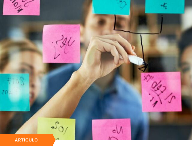 Portada de artículo que muestra un primer plano de un profesional organizando un flujo de trabajo con notas adhesivas en un panel, con etiqueta naranja de ARTÍCULO en la esquina inferior.
