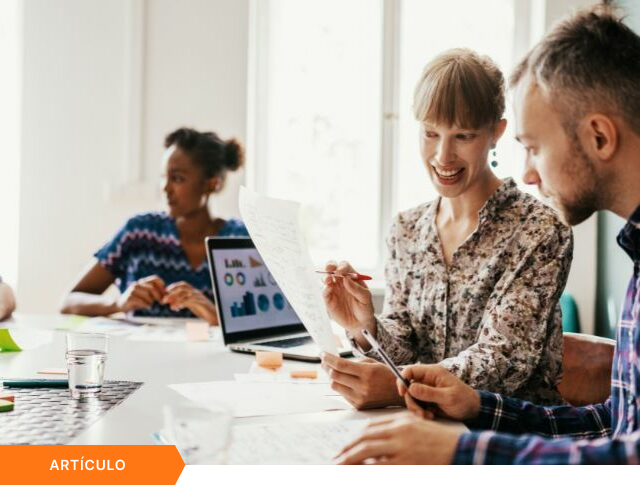 Imagen de portada para artículo mostrando a dos profesionales sonriendo mientras analizan un documento impreso, con una laptop exhibiendo gráficos de rendimiento al fondo y una etiqueta naranja de ARTÍCULO en la esquina inferior izquierda.