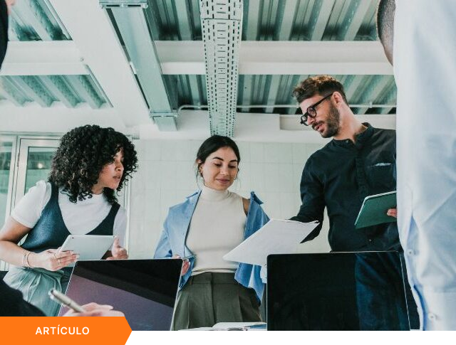 Imagen de portada para artículo mostrando a un equipo diverso de profesionales colaborando en una oficina de estilo industrial, con una etiqueta naranja que dice ARTÍCULO en la esquina inferior izquierda.