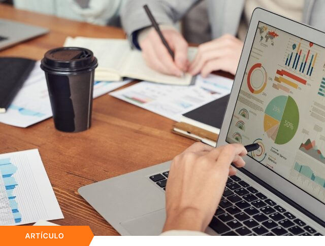 Imagen de portada para artículo mostrando el primer plano de un profesional señalando gráficos de rendimiento en la pantalla de una laptop, mientras un colega toma notas al fondo, con una etiqueta naranja de ARTÍCULO en la esquina inferior izquierda.