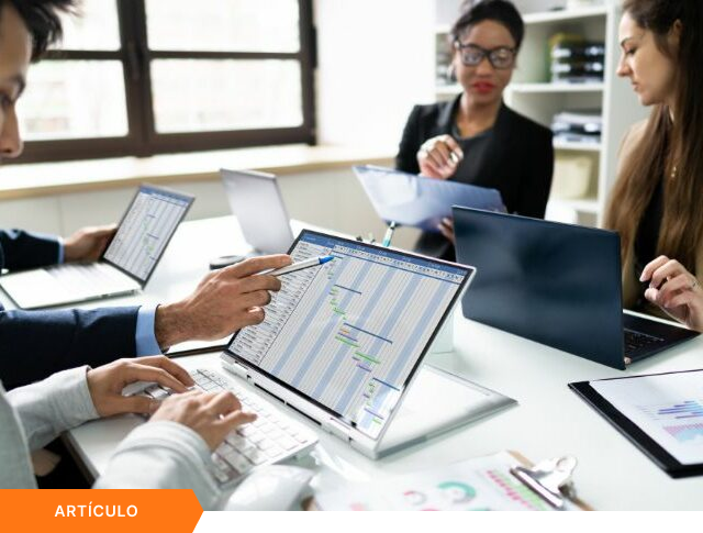 Imagen de portada para artículo mostrando a un equipo multidisciplinario analizando un diagrama de Gantt en una laptop convertible durante una sesión de trabajo, con una etiqueta naranja de ARTÍCULO en la esquina inferior izquierda.