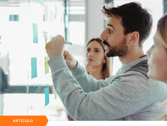 Imagen de portada para artículo mostrando a un equipo creativo trabajando con notas adhesivas en un panel de vidrio durante una sesión de ideación, con una etiqueta naranja de ARTÍCULO en la esquina inferior izquierda.