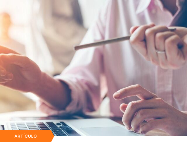 Imagen de portada para artículo mostrando un primer plano de las manos de dos profesionales colaborando estrechamente frente a una laptop bajo una luz cálida, con una etiqueta naranja de ARTÍCULO en la esquina inferior izquierda.