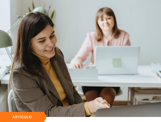 Portada de artículo que muestra a dos mujeres profesionales colaborando en una oficina moderna con laptops, con la etiqueta naranja de ARTÍCULO en la esquina inferior izquierda.