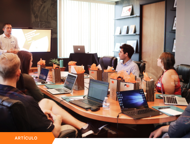 Portada de artículo que muestra a un ponente dando una charla de capacitación sobre desarrollo y diseño a un equipo de trabajo en una sala de reuniones, con etiqueta naranja de ARTÍCULO en la esquina inferior.