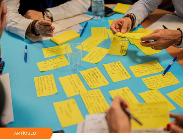 Portada de artículo que muestra una vista superior de un equipo organizando notas adhesivas en una mesa azul durante un taller, con etiqueta naranja de ARTÍCULO en la esquina inferior.