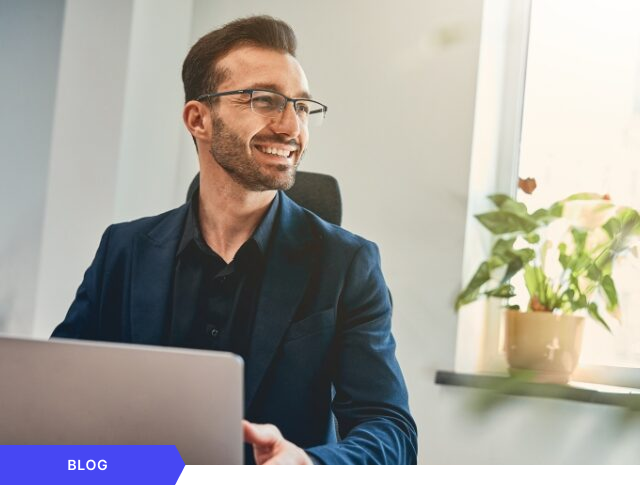 Profesional de gestión de proyectos trabajando sonriente en su laptop en una oficina moderna, utilizado como imagen de portada para un artículo de blog sobre productividad y éxito en la ejecución de estrategias de innovación.