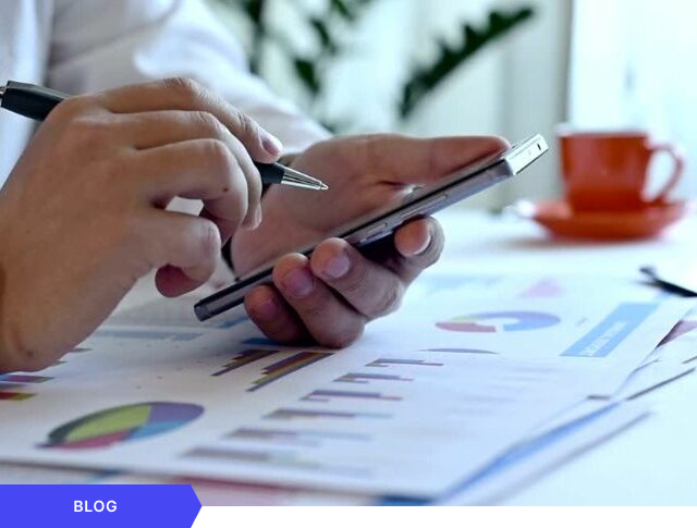 Primer plano de un profesional analizando métricas de rendimiento y gráficos utilizando su smartphone y documentos impresos, diseñado como imagen de portada para un artículo de blog sobre seguimiento de datos y agilidad en la gestión de proyectos.