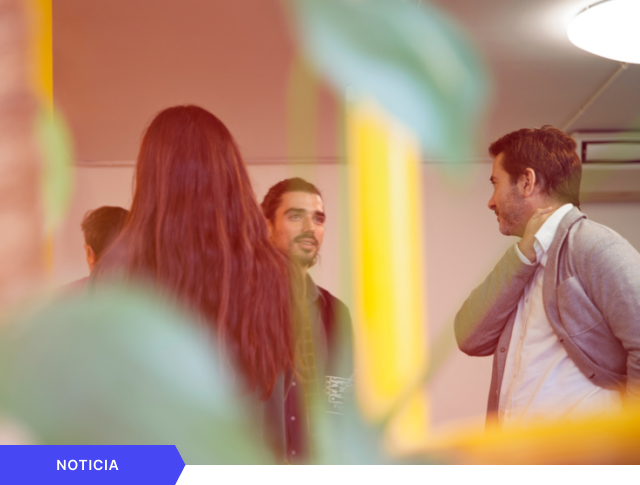 Portada de noticia que muestra a varios profesionales conversando en una oficina con un filtro cálido y desenfoque de primer plano, con etiqueta azul de NOTICIA en la esquina inferior.
